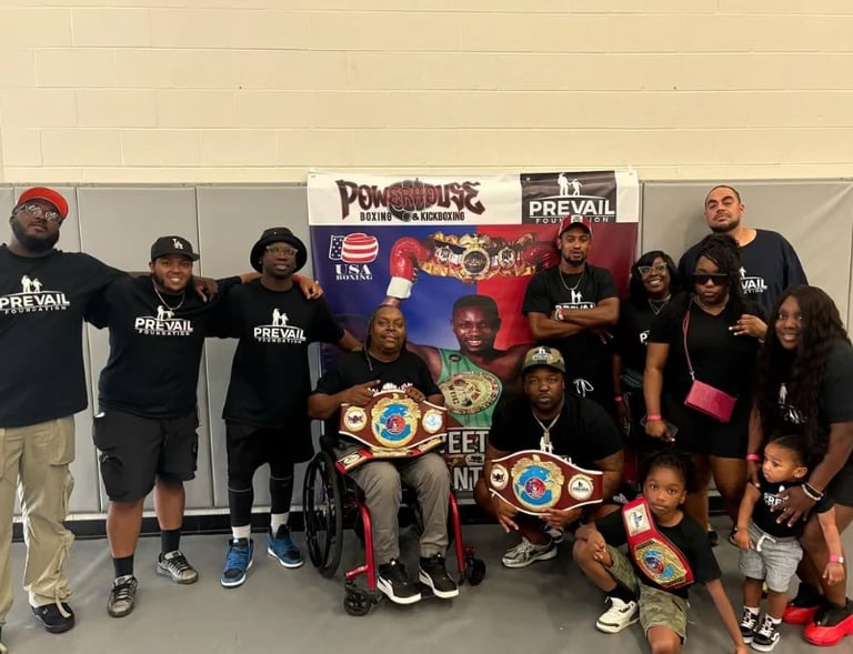 Group of people wearing black PREVAIL shirts posing together indoors, with championship belts displayed