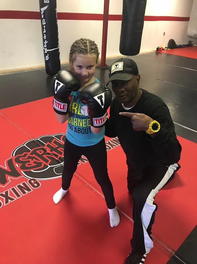 Young girl in boxing gloves with trainer in boxing gym on red mat floor